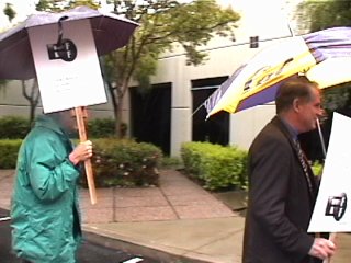 [Pic: protestors marching with signs & umbrellas outside FCC office]